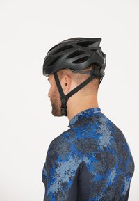 Sort cykelhjelm med aerodynamisk design, der har flere ventilationshuller og justerbar hage-rem. Bæres med en blå og grå mønstret skjorte.