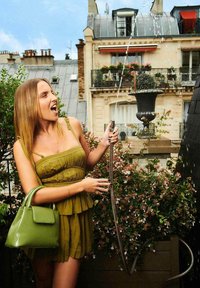 Vestito peplum verde con spalline sottili e textura ondulata, abbinato a una borsa verde lucida. Spruzzi d'acqua da un ugello tenuto in una mano.