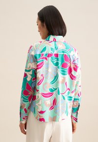 Blumenhemd mit knöpfen in lebhaften Mustern aus Pink, Türkis und Cremeton, mit abgerundetem Saum und langen Ärmeln. Leichter Stoff.