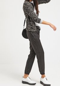 Svarta, lätta, smalnande joggerbyxor med elastisk midja. Vita, tjocka skor med dragkedjeaccent. Texturerad svart- och vit cardigan.