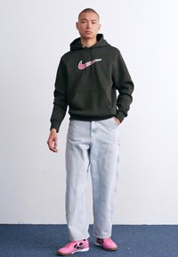 Sort hættetrøje med et pink Nike-logo, parret med lyseblå baggy jeans og pink sneakers. Enkel design, afslappet pasform.