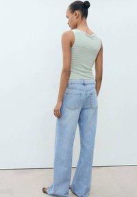 Striped tank top in green and cream, paired with light blue wide-leg jeans. Jeans feature a classic five-pocket design and slight fade.