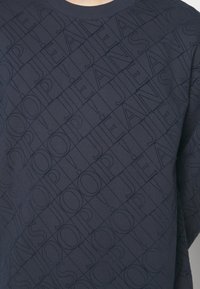 Felpa blu navy con motivo logo testurizzato in un design a griglia a rombi. Presenta un collo a coste e maniche lunghe. Materiale misto cotone.