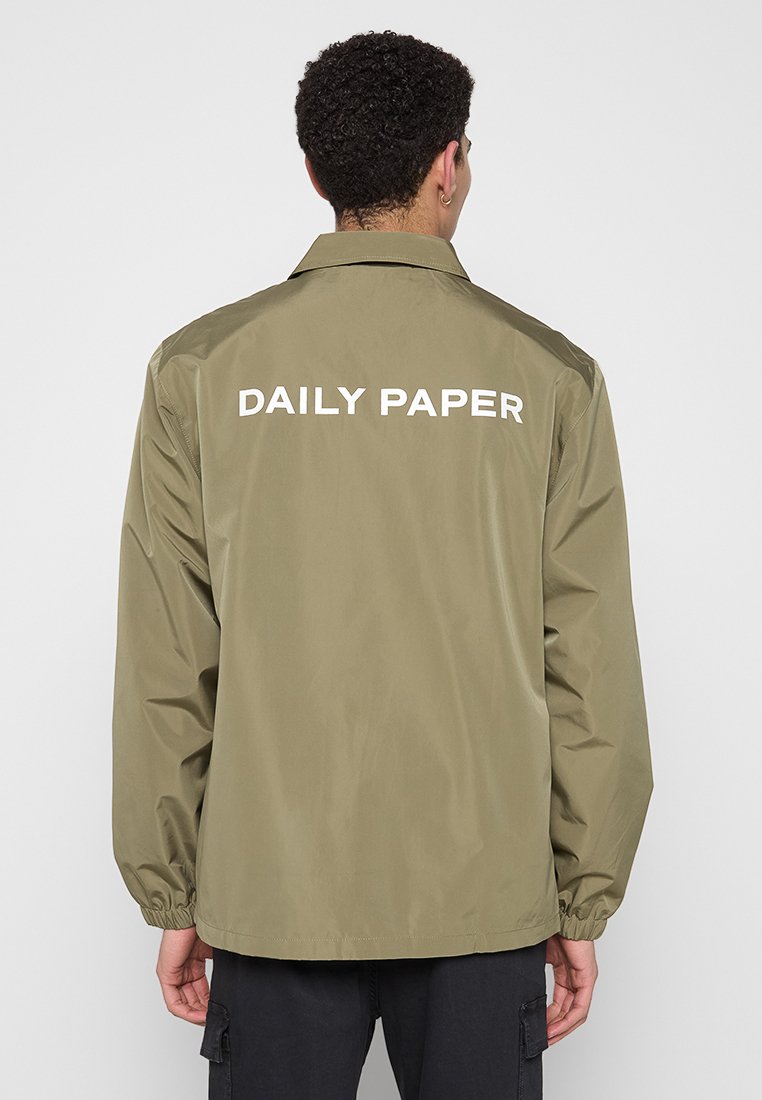 Olijfgroen, lichtgewicht jack met een klassieke kraag en elastische manchetten. Voorzien van grote "DAILY PAPER" tekst in het wit gedrukt op de achterkant.
