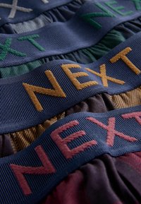 Bawełniane opaski w różnych kolorach z haftowanym napisem "NEXT" w kontrastującym kolorze nici. Opaski mają wzory w paski i kratę.