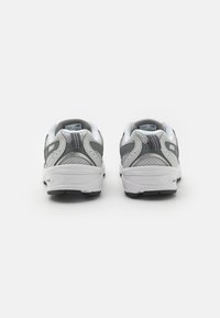 Baskets de sport grises et blanches avec une tige en maille, un col rembourré et une semelle extérieure texturée. Comprend des détails de logo et d'accentuation sur le talon.