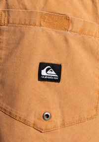 Tela naranja con una superficie texturizada que presenta una etiqueta negra de Quiksilver y un ojete metálico en un bolsillo.
