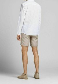 Valkoinen pitkähiha-paita, jossa on pieniä sinisiä ja punaisia pisteitä, yhdistettynä beigen värisiin shortseihin. Ruskeat mokkasaapikkaat täydentävät asun.