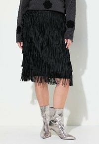 Jupe noire à franges avec une texture superposée, associée à des bottines argentées brillantes. Complétée par un pull gris confortable avec des accents floraux.
