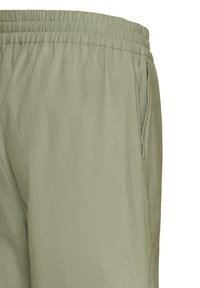 Pantalon vert olive clair avec taille élastique et poche latérale, visible de la taille jusqu'à mi-cuisse.