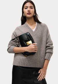 Maglione beige a collo a V con orlo a coste, abbinato a una borsa a tracolla in pelle nera con una chiusura rettangolare dorata.