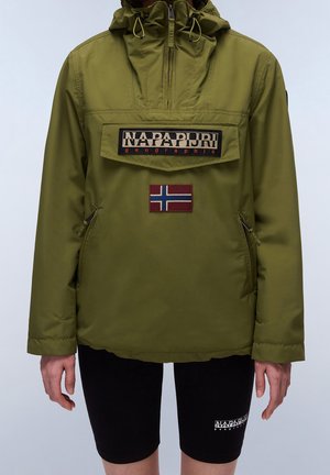 Osoba nosząca oliwkową kurtkę Napapijri z przednią kieszenią na klapę i naszywką z flagą Norwegii, w połączeniu z czarnymi szortami z logo Napapijri.