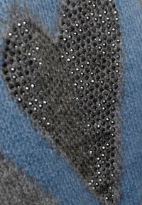 Blaues Gewebe mit einem Herzmuster, das schwarze glänzende Nieten vor einem strukturierten grauen Hintergrund zeigt. Die Materialien sind weich und flauschig.