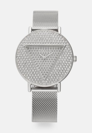Montre en argent avec un cadran rond présentant une surface texturée de cristaux clairs en forme triangulaire. Le bracelet est en maille métallique tissée.