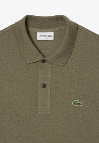 Camisa polo verde oliva, corte slim, tejido texturizado, cuello acanalado, dos botones negros, con un logo de cocodrilo bordado en el lado izquierdo del pecho.