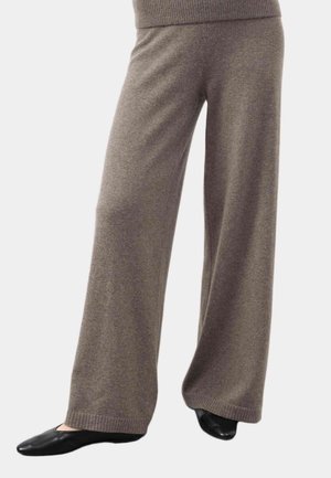 Pantaloni morbidi a gamba larga di colore marrone, indossati con scarpe slip-on nere, mostrati dalla vita ai piedi su uno sfondo semplice.