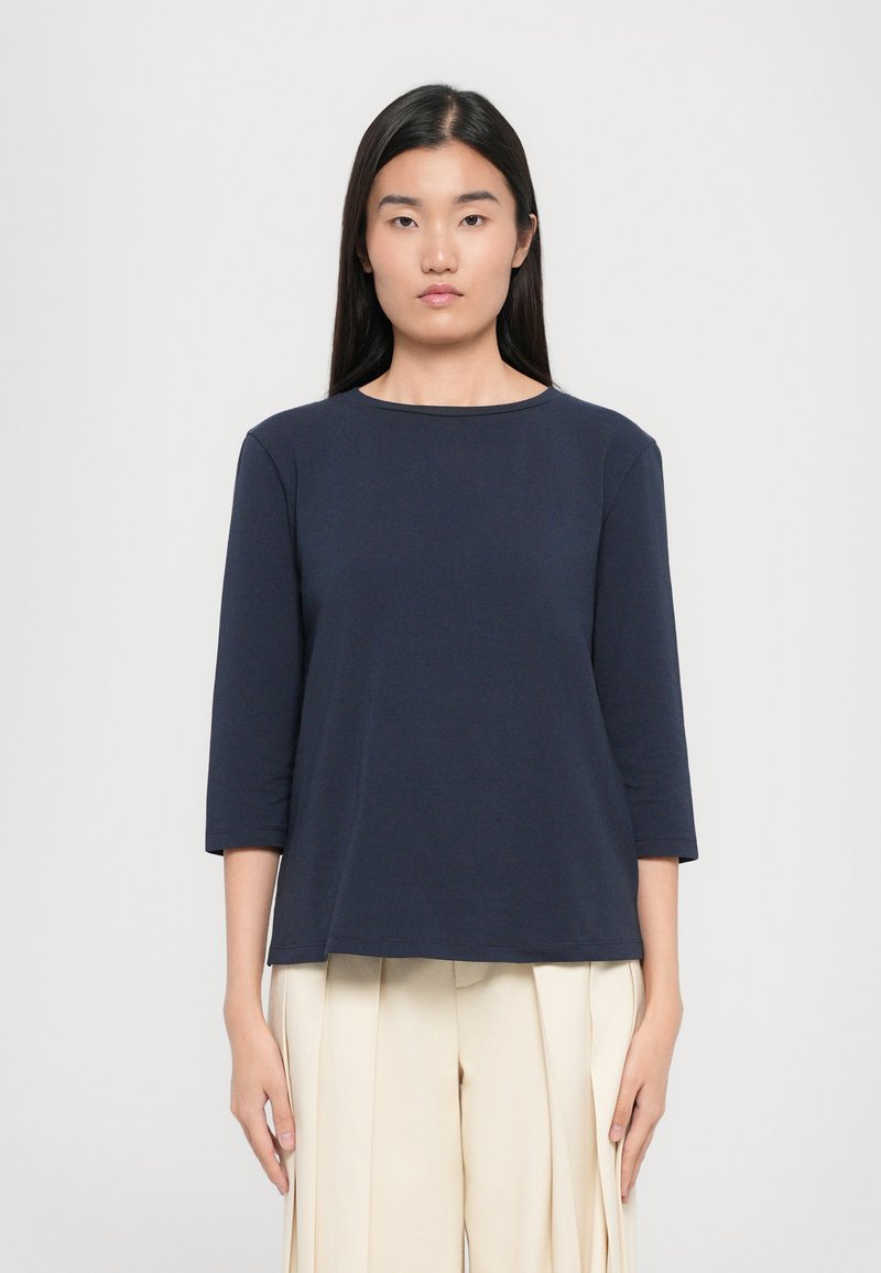 Top blu navy a tre quarti in morbido tessuto. Presenta un colletto rotondo e una vestibilità comoda, abbinato a pantaloni pieghettati di colore chiaro.