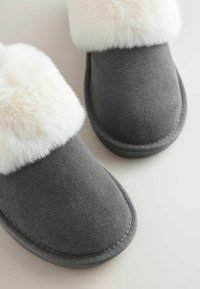 Gray slippers with a soft white faux fur cuff, made of textured material, featuring a rounded toe and stitched detailing along the sole.