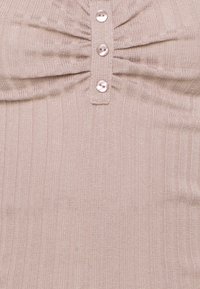 Tissu en maille côtelée beige clair avec un détail froncé et trois boutons brillants alignés verticalement.