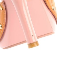 Gros plan sur une chaussure à talon haut rose montrant la pointe du talon et une partie de la semelle avec des détails en cuir beige et des clous dorés.