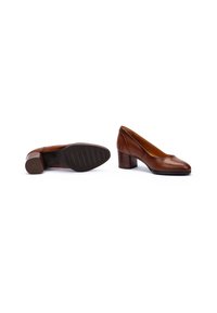 Une paire de chaussures pour femmes en cuir marron à petit talon, l'une debout et l'autre sur le côté montrant la semelle en caoutchouc noire avec des rainures.
