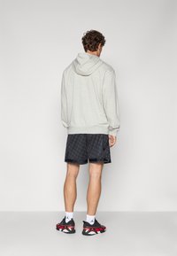 Grå hætte sweatshirt med snørre, parret med sorte mønstrede shorts. Outfittet er suppleret af rød og sort sportssko.