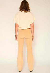 Haut de couleur crème avec une coupe décontractée, associé à un pantalon évasé en velours côtelé beige taille haute, doté de poches arrière et d'une texture lisse.