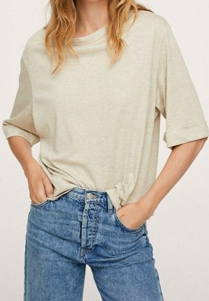 T-shirt beige clair à coupe décontractée avec manches retroussées, associée à un jean en denim bleu taille haute. Texture de tissu douce ; design décontracté.