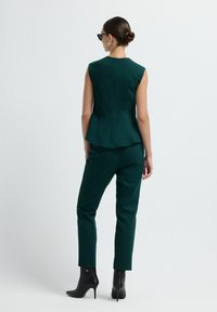 Turkusowy top bez rękawów z peplum, zestawiony z dopasowanymi turkusowymi spodniami i czarnymi botkami na obcasie. Gładka tkanina, minimalne szwy.
