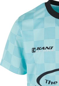 Gaiši zils sporta krekls ar pārbaudītu rakstu, melnu apkakli un "KANI SPORT" logotipu. Audums šķiet struktūrēts ar elpojošu dizainu.