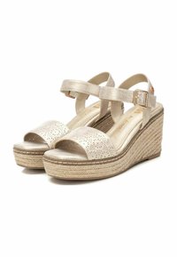 Sandali con zeppa in materiale dorato metallizzato, caratterizzati da motivi floreali ritagliati, cinturino alla caviglia con fibbia e suola con piattaforma in stile juta intrecciata.