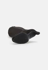 Bottine en suede noire avec une finition lisse, une fermeture éclair discrète sur le côté et une semelle en caoutchouc texturée pour une meilleure adhérence.
