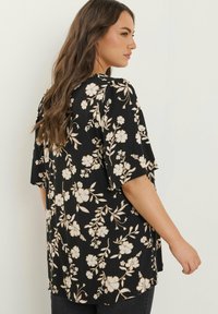 Sort bluse med blomsterdesign i beige, korte ærmer, løs pasform og rund halsudskæring. Blødt, let stof for komfort.