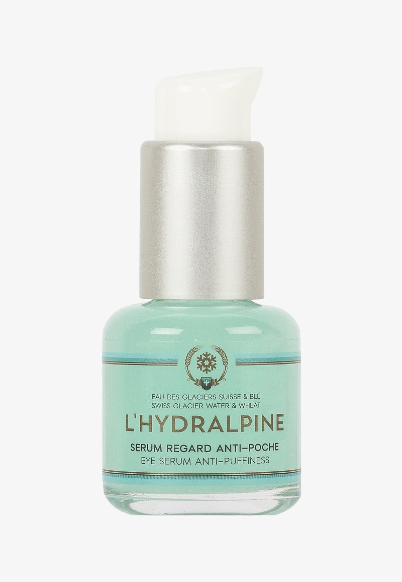 Bouteille en verre clair contenant un sérum pour les yeux bleu clair avec un distributeur à pompe argenté. L'étiquette présente du texte en doré et en bleu.