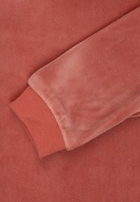 Korálový svetrový materiál s jemnou textúrou. Obsahuje pletený lem v zodpovedajúcej farbe. Viditeľné švy v blízkosti lemu.
