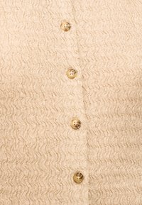 Tissu beige texturé présentant un motif ondulé avec quatre boutons marron clair uniformément espacés en une rangée verticale.