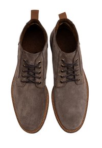 Brązowe zamszowe buty z okrągłym czubkiem, sznurowane, z złotymi oczkami i kontrastującą jasnobrązową podeszwą. Posiadają uchwyt na pięcie.