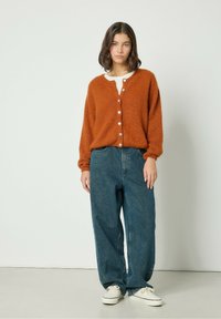 Kollane, lopsakas kardigan nööpidega, mis on koos lõdva sinise teksapüksiga ja valgete tossudega. Lihtne, mugav lõige ja tekstureeritud kangas.