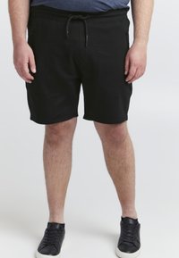 Shorts noirs avec une taille élastique et un cordon de serrage, dotés de poches zippées sur les côtés et d'un tissu doux et texturé. Associés à des baskets noires.