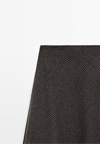 Petit morceau de tissu à carreaux gris foncé et noir sur fond blanc, montrant la texture et les détails fins du motif.