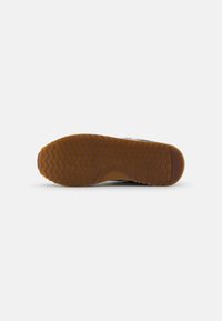 Rubber sole with a wavy pattern, tan color. The upper section is grey with textured accents, showcasing a rounded design.