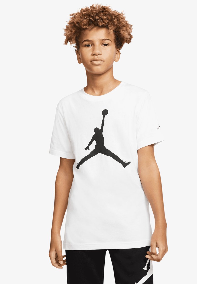 Λευκό βαμβακερό T-shirt με μεγάλο μαύρο λογότυπο Jumpman στο μπροστινό μέρος. Μανίκια κοντά και στρογγυλή λαιμόκοψη, συνδυασμένο με μαύρο παντελόνι.