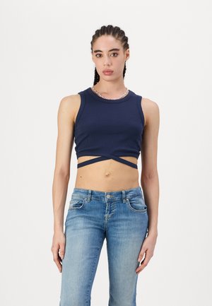 Top corto de tirantes azul marino con un acabado texturizado, que presenta tirantes cruzados en la cintura. Combinado con jeans de pierna recta de lavado claro.