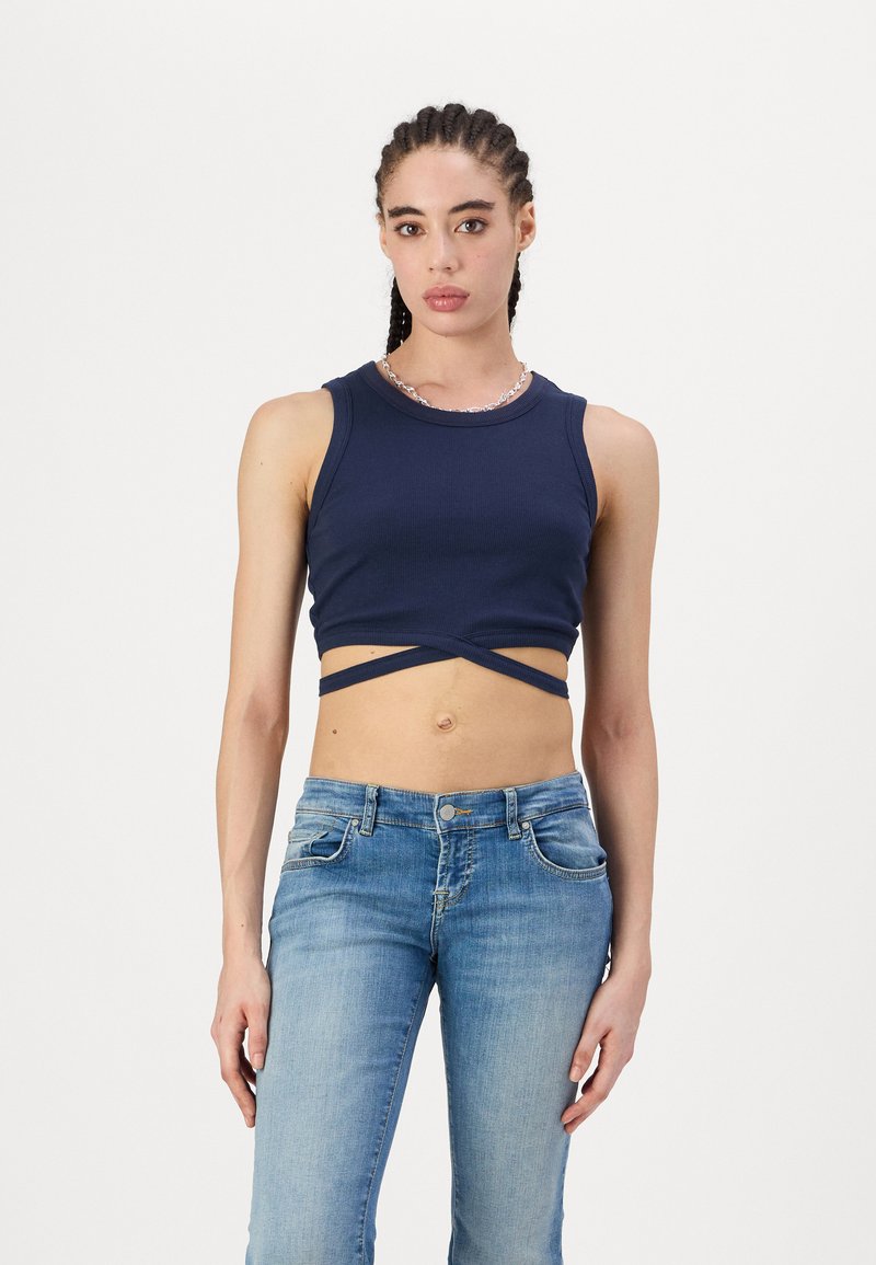 Sötétkék, rövidített tank top, texturált felülettel, keresztben elhelyezett pántokkal a deréknál. Világos mosású, egyenes lábú farmernadrággal párosítva.