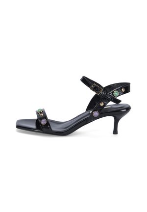 Sandale à talon kitten en cuir verni noir avec bride de cheville, bout carré, clous dorés et ornements de pierres précieuses vertes et violettes.
