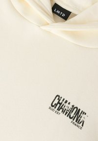 Kreemikas kapuutsiga dressipluus musta tekstiga „CHÂMONT” ja väiksema kirjaga „SUD EST FRANCE” trükitud rinnal kaeluse all, musta LMTD sildiga.