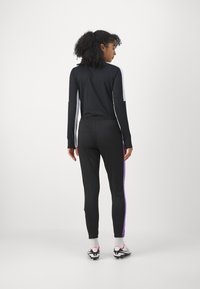 Chándal atlético negro con mangas largas y franjas laterales moradas. Presenta un diseño ajustado y cintura elástica, fabricado con material ligero.