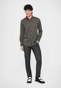 Crna košulja s uzorkom i dugim rukavima, uparena s tamnim trapericama i crnim cipelama s bijelim detaljima.