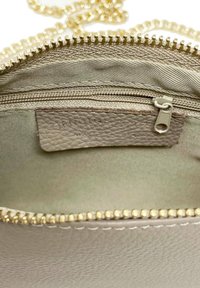 Interno di una borsa in pelle beige con zip dorata, caratterizzata da una piccola tasca con zip e foderatura in tessuto liscio. La tracolla a catena è visibile.