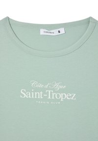 T-shirt in cotone verde chiaro con scollatura a girocollo e testo bianco: "Côte d'Azur Saint-Tropez TENNIS CLUB." Etichetta della taglia indica small.